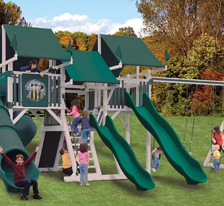 A group of children playing on a green and white outdoor playset with slides, ladders, and a tube. Trees and a blue sky are visible in the background.