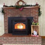 A brick fireplace with a black wood-burning stove is decorated with a clock, candles, greenery, and a wooden crate with ornaments and flowers.