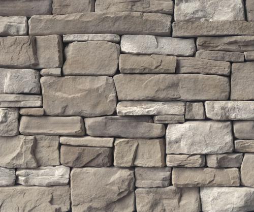 Close-up image of a stone wall made of variously sized rectangular and square stones. The stones are shades of brown and gray, stacked in an irregular pattern.