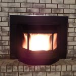 A black pellet stove with a bright flame inside is set against a brick fireplace, providing warmth and comfort.