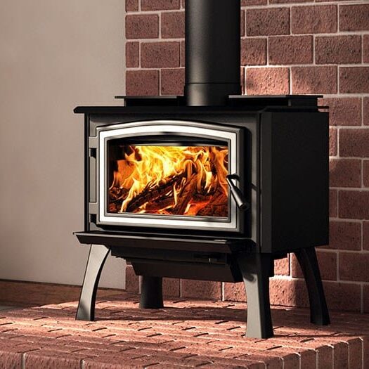 A black wood-burning stove with a glass door, emitting flames, stands on a brick base against a brick wall background.